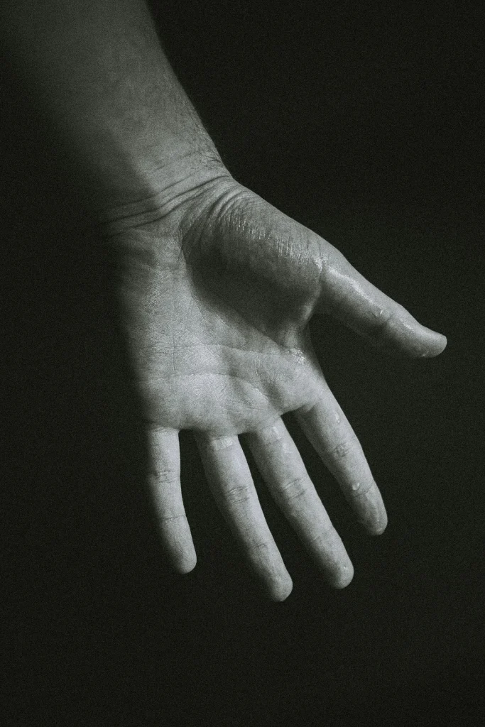 Close black-and-white photo of an open hand reaching from shadow — history of masturbation shame essay, 49Grey