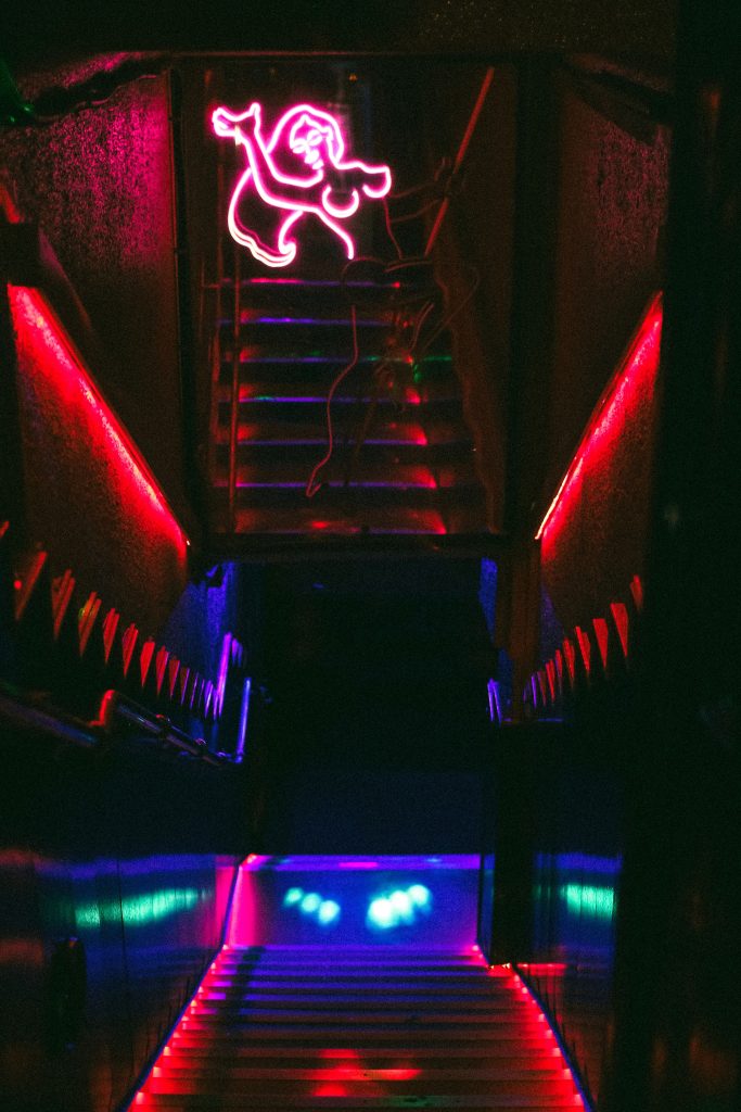 Neon dancer over a staircase leading down to the dance floor of a dark nightclub