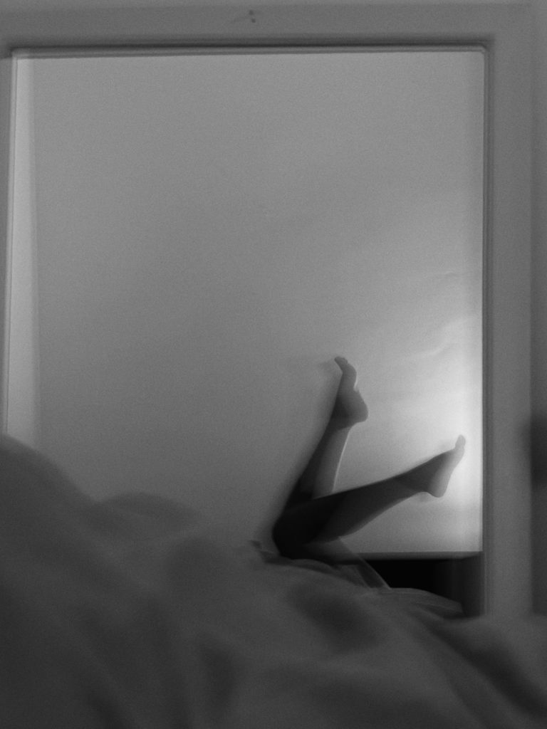 Black-and-white silhouette of raised bare legs lit against a window — body count shame essay, 49Grey
