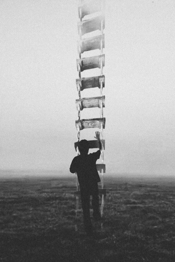 Silhouetted figure reaching toward an impossibly tall ladder into fog. 49Grey introduction essay, living in the grey