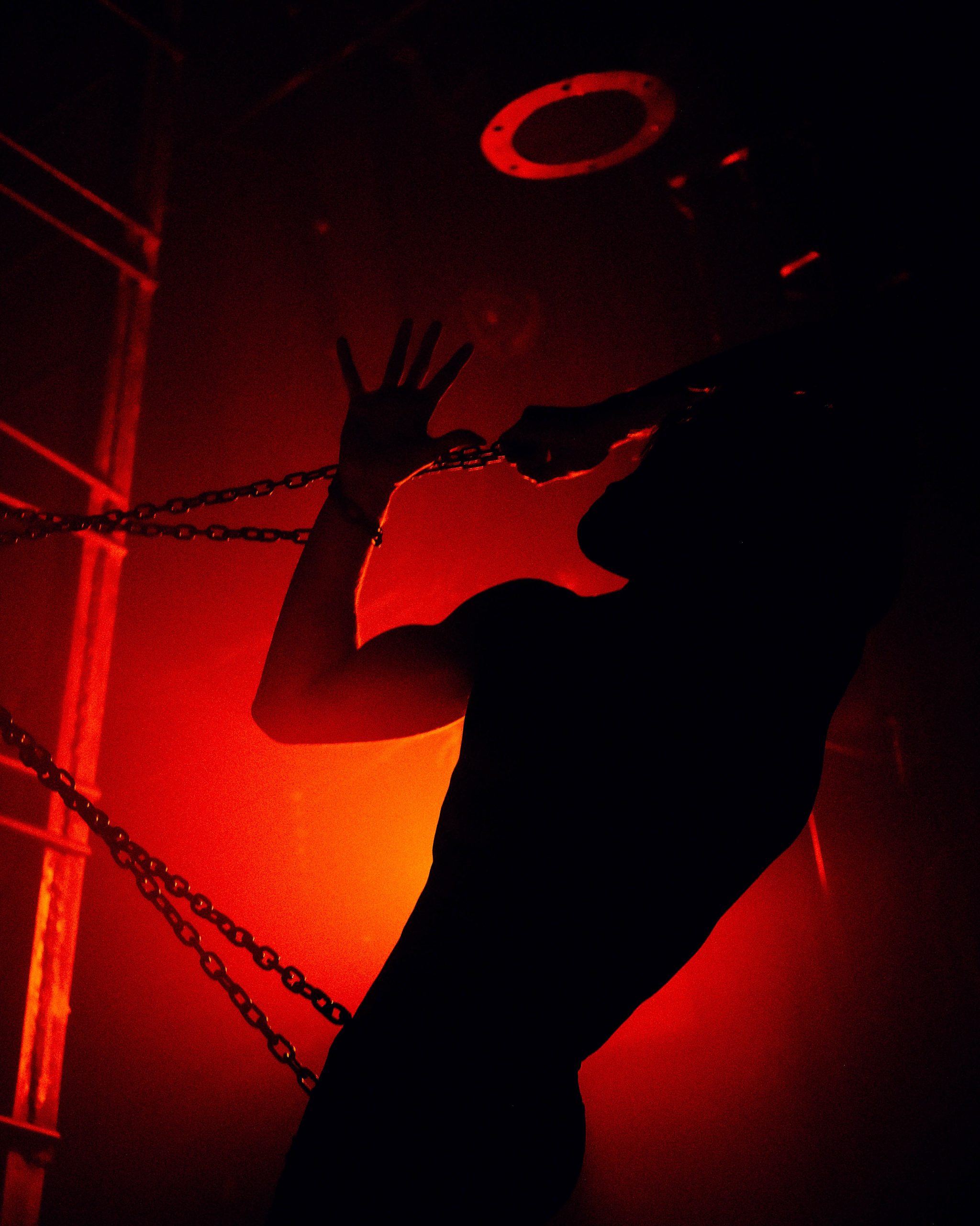 Silhouetted figure gripping chains under red haze in a gay bar setting — gay bar exclusivity essay, 49Grey