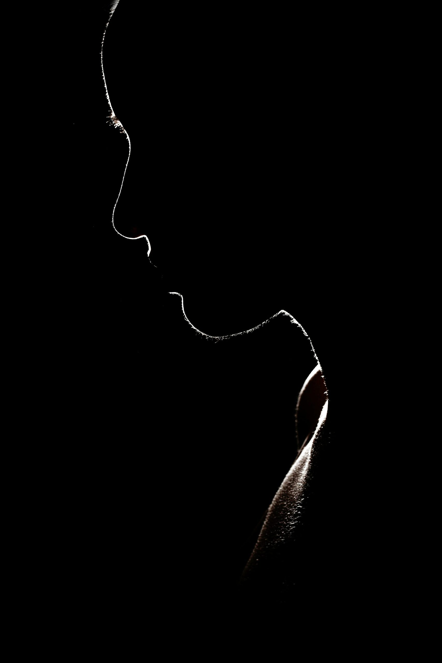 Rim-lit silhouette of a face and shoulder emerging from darkness. Kink curious beginners essay, 49Grey