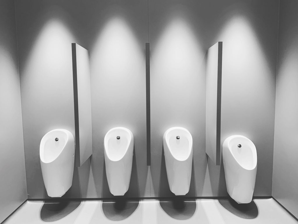 Rows of white urinals under dramatic spotlights in black and white — George Michael cruising culture essay, 49Grey